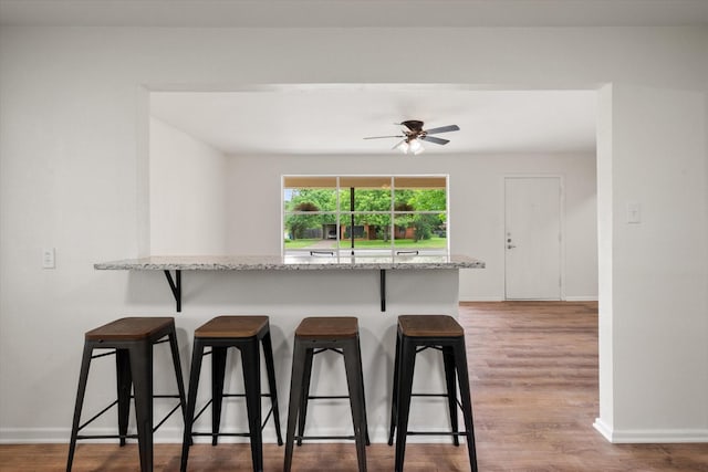 2040 Bowie Dr, Corsicana, TX 75110 - kitchen featuring a kitchen breakfast bar, light stone counters, ceiling fan, and light wood finished floors