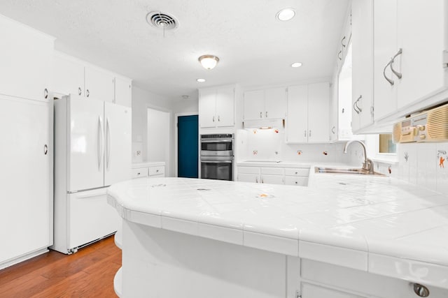 2333 Hermanson Dr, Waco, TX 76710 - kitchen with freestanding refrigerator, stainless steel double oven, tile counters, light wood-type flooring, and a peninsula