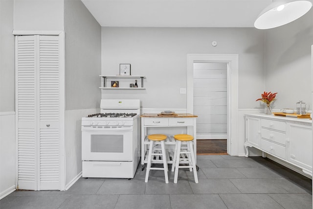 2700 Ethel Ave, Waco, TX 76707 - kitchen featuring white gas range oven, tile patterned flooring, light countertops, and a wainscoted wall