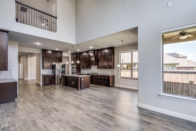 6105 Horsetail Dr, Mckinney, TX 75071 - kitchen with stainless steel fridge with ice dispenser, dark brown cabinetry, a center island with sink, light countertops, and premium range hood