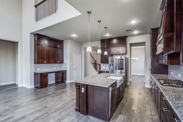 6105 Horsetail Dr, Mckinney, TX 75071 - kitchen featuring stainless steel appliances, tasteful backsplash, wood finished floors, dark brown cabinetry, and a kitchen island with sink
