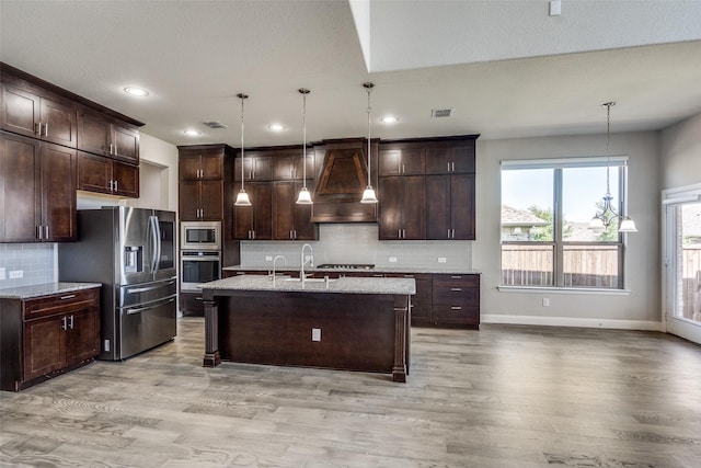 6105 Horsetail Dr, Mckinney, TX 75071 - kitchen featuring custom range hood, stainless steel appliances, dark brown cabinets, light wood-style floors, and tasteful backsplash