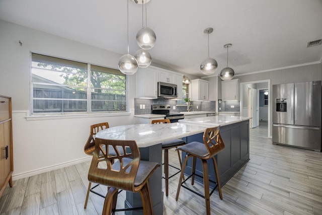 1203 Woodridge Cir, Euless, TX 76040 - kitchen featuring appliances with stainless steel finishes, a center island, backsplash, white cabinets, and decorative light fixtures
