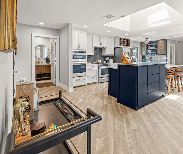 6005 Costera Ln, Dallas, TX 75248 - kitchen featuring appliances with stainless steel finishes, a skylight, white cabinetry, backsplash, and recessed lighting