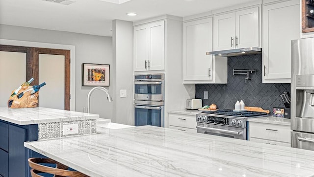 6005 Costera Ln, Dallas, TX 75248 - kitchen with stainless steel appliances, white cabinetry, under cabinet range hood, backsplash, and recessed lighting