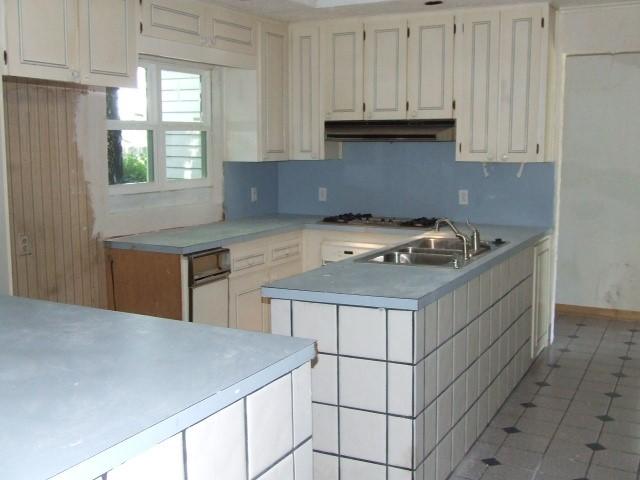 1729 Lindy Ln, Irving, TX 75060 - kitchen featuring under cabinet range hood, stainless steel gas cooktop, light countertops, white cabinetry, and a peninsula