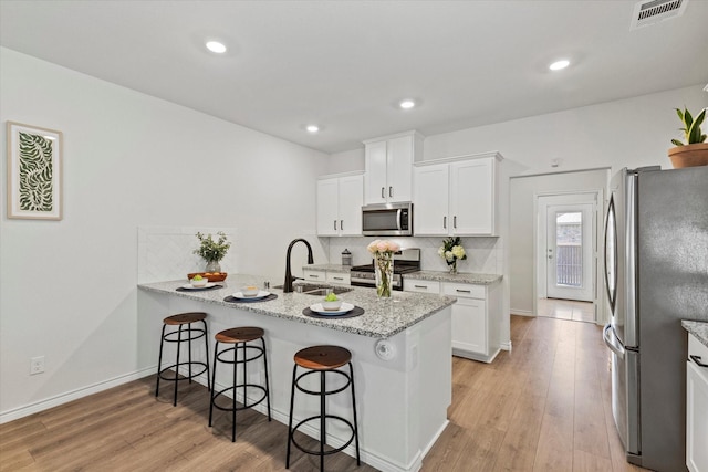 1512 Bennington Ln, Celina, TX 75009 - kitchen with appliances with stainless steel finishes, a peninsula, a kitchen breakfast bar, light wood-style floors, and white cabinets