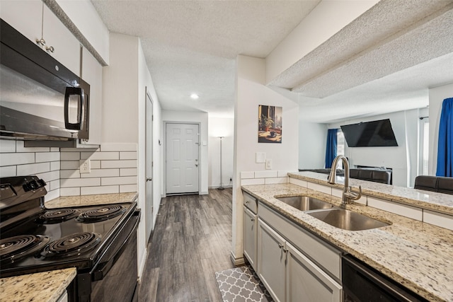 6050 Melody Ln Unit 107, Dallas, TX 75231 - kitchen with black appliances, a textured ceiling, dark wood finished floors, tasteful backsplash, and light stone counters