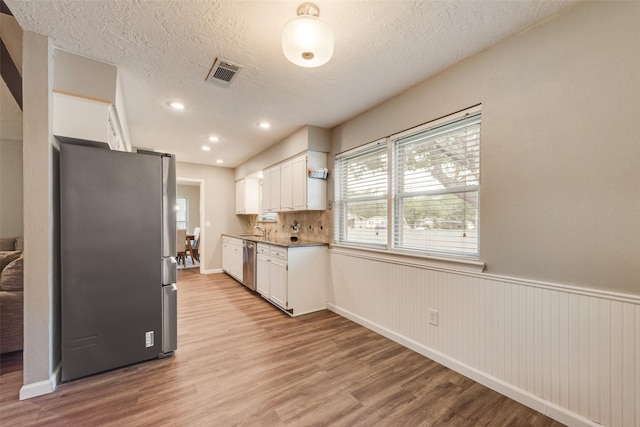 640 Silverstone Dr, Richardson, TX 75080 - kitchen featuring appliances with stainless steel finishes, light wood-type flooring, white cabinetry, wainscoting, and a textured ceiling