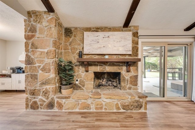 640 Silverstone Dr, Richardson, TX 75080 - unfurnished living room featuring beam ceiling, wood finished floors, a stone fireplace, and a textured ceiling