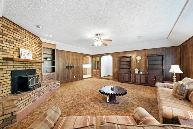 7220 Tucker Dr, Weatherford, TX 76085 - living area with wooden walls, a textured ceiling, a ceiling fan, a wood stove, and carpet