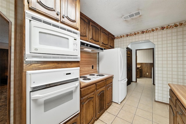 7220 Tucker Dr, Weatherford, TX 76085 - kitchen featuring white appliances, under cabinet range hood, wallpapered walls, a textured ceiling, and light tile patterned flooring