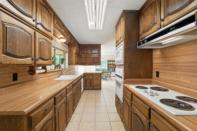 7220 Tucker Dr, Weatherford, TX 76085 - kitchen with white appliances, under cabinet range hood, light tile patterned floors, a textured ceiling, and wood walls