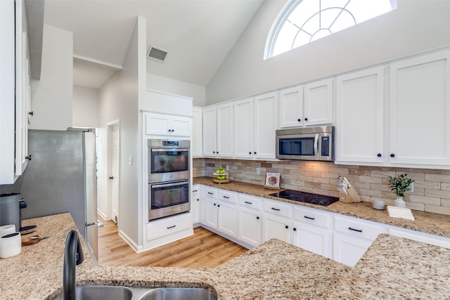 8600 Digby Dr, Plano, TX 75025 - kitchen featuring appliances with stainless steel finishes, high vaulted ceiling, light wood finished floors, white cabinetry, and tasteful backsplash