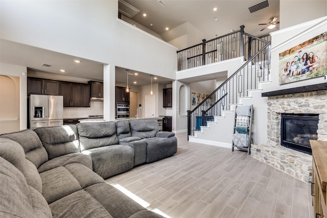 11825 Wulstone Rd, Fort Worth, TX 76052 - living room with a stone fireplace, ceiling fan, a towering ceiling, light wood finished floors, and stairway