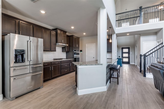 11825 Wulstone Rd, Fort Worth, TX 76052 - kitchen featuring stainless steel appliances, dark brown cabinetry, light stone countertops, light wood-style flooring, and a high ceiling