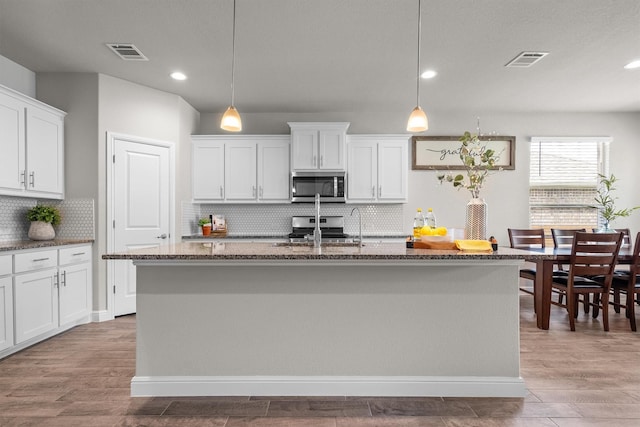 171 Tanager Dr, Rhome, TX 76078 - kitchen with appliances with stainless steel finishes, dark stone countertops, a center island with sink, light wood-style floors, and white cabinets