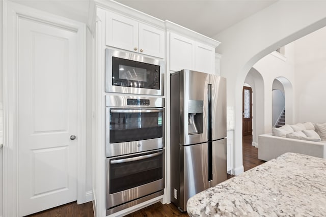 2751 Langley Way, Prosper, TX 75078 - kitchen featuring appliances with stainless steel finishes, arched walkways, white cabinetry, light stone counters, and dark wood-type flooring