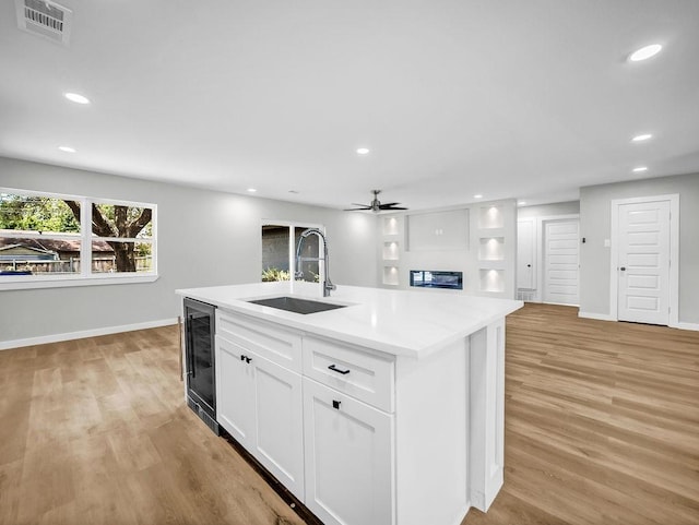 3505 Morningstar Ln, Farmers Branch, TX 75234 - kitchen featuring wine cooler, light wood finished floors, a ceiling fan, white cabinets, and a kitchen island with sink