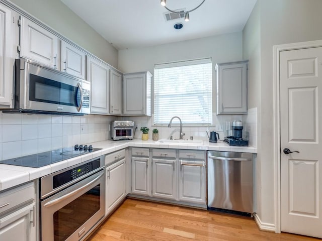 6505 Tamarron Ln, Plano, TX 75024 - kitchen featuring stainless steel appliances, light wood-style flooring, decorative backsplash, tile countertops, and gray cabinetry