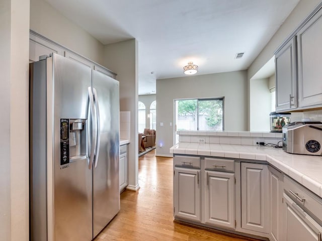 6505 Tamarron Ln, Plano, TX 75024 - kitchen featuring stainless steel refrigerator with ice dispenser, gray cabinetry, light wood-type flooring, and tile countertops