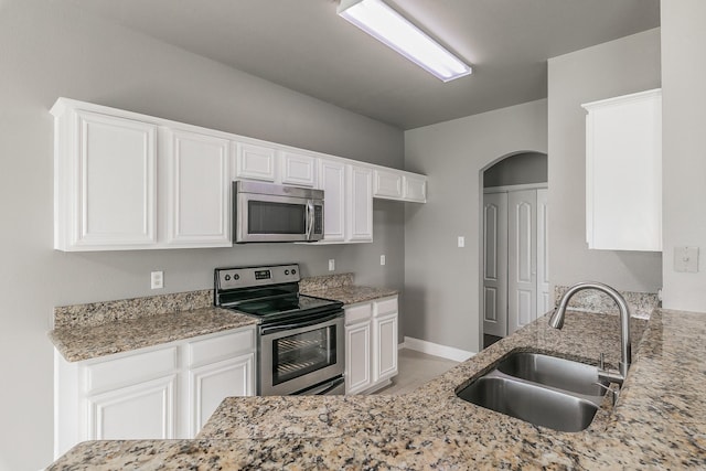 1102 David Dr, Euless, TX 76040 - kitchen featuring stainless steel appliances, light stone counters, white cabinets, and arched walkways