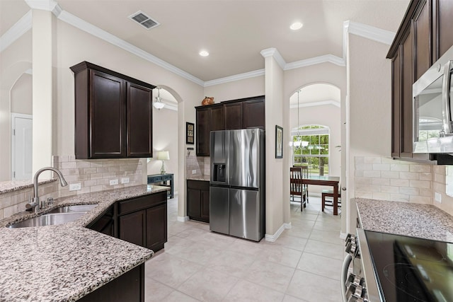 11513 Champion Creek Dr, Frisco, TX 75036 - kitchen featuring appliances with stainless steel finishes, arched walkways, light stone counters, dark brown cabinetry, and backsplash