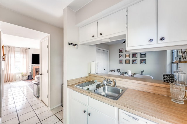 1161 Dallas Dr, Denton, TX 76205 - kitchen with white dishwasher, light tile patterned flooring, light countertops, white cabinetry, and a fireplace