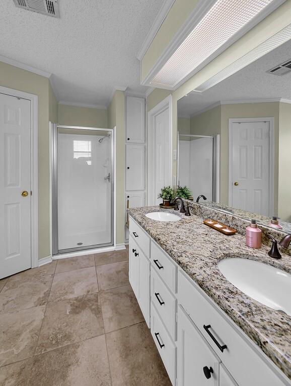 11001 Ridge Point Dr, Woodway, TX 76712 - bathroom with a stall shower, double vanity, a textured ceiling, ornamental molding, and tile patterned floors