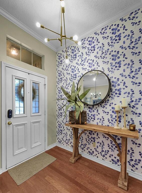 11001 Ridge Point Dr, Woodway, TX 76712 - foyer entrance with a chandelier, wallpapered walls, ornamental molding, a textured ceiling, and wood finished floors
