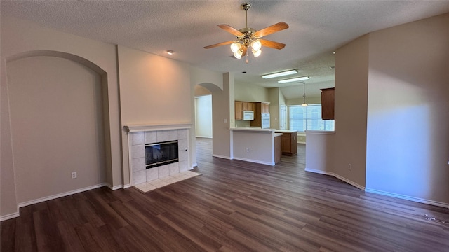 2217 Lone Pecan Dr, Garland, TX 75040 - unfurnished living room featuring arched walkways, dark wood finished floors, a ceiling fan, a textured ceiling, and a tile fireplace