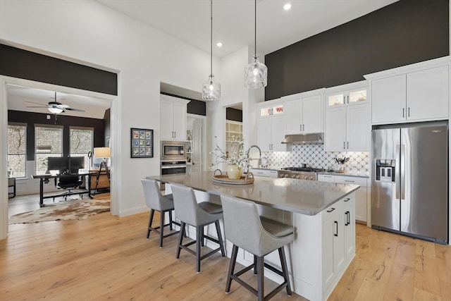 204 Big Sky Cir, Northlake, TX 76226 - kitchen with appliances with stainless steel finishes, under cabinet range hood, decorative backsplash, light wood-style flooring, and a center island with sink