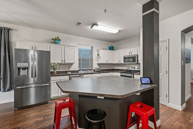 13341 Ridgepointe Rd, Fort Worth, TX 76244 - kitchen featuring stainless steel appliances, dark countertops, dark wood-style floors, white cabinetry, and a kitchen bar