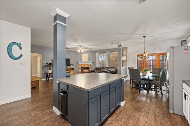 13341 Ridgepointe Rd, Fort Worth, TX 76244 - kitchen featuring ceiling fan, a warm lit fireplace, freestanding refrigerator, dark wood-type flooring, and decorative columns