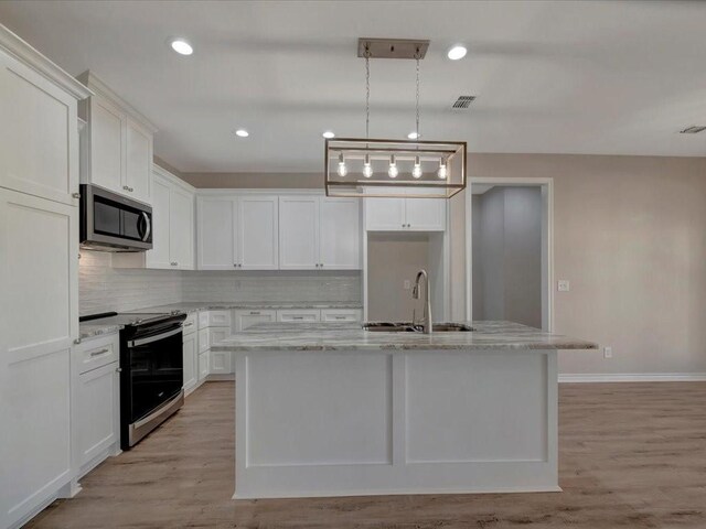 106 Saddle Brook Dr, Lufkin, TX 75904 - kitchen with stainless steel microwave, range with electric stovetop, backsplash, white cabinets, and an island with sink