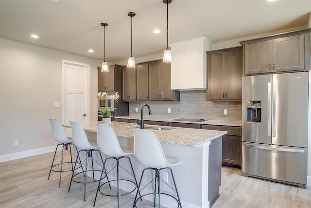 619 Latigo Ct, Weatherford, TX 76088 - kitchen featuring stainless steel fridge with ice dispenser, light wood-style floors, decorative backsplash, a kitchen bar, and a center island with sink