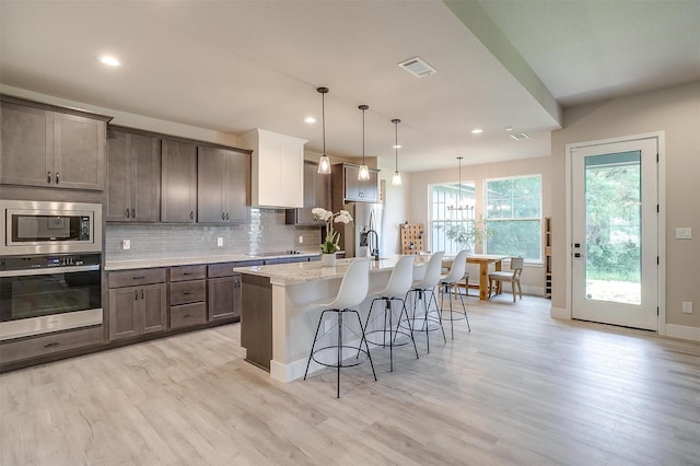 619 Latigo Ct, Weatherford, TX 76088 - kitchen featuring stainless steel appliances, light wood-style floors, a breakfast bar area, a kitchen island with sink, and tasteful backsplash