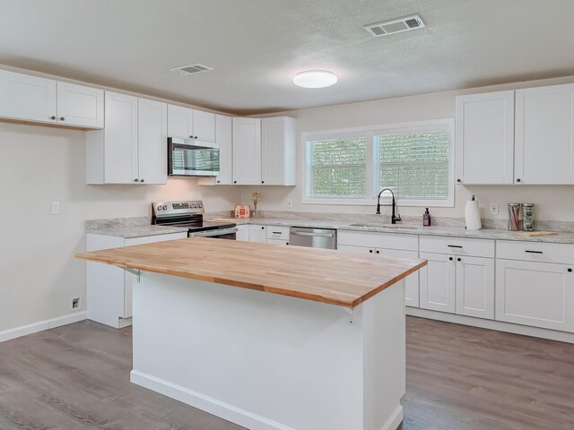 1605 N Beaton St, Corsicana, TX 75110 - kitchen featuring stainless steel appliances, butcher block countertops, light wood-style flooring, white cabinetry, and a textured ceiling
