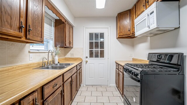217 Wintercrest Rd, Burleson, TX 76028 - kitchen featuring black gas stove, white microwave, brown cabinetry, tasteful backsplash, and light countertops