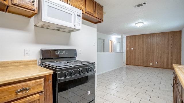 217 Wintercrest Rd, Burleson, TX 76028 - kitchen with black gas range oven, white microwave, light countertops, brown cabinetry, and a textured ceiling