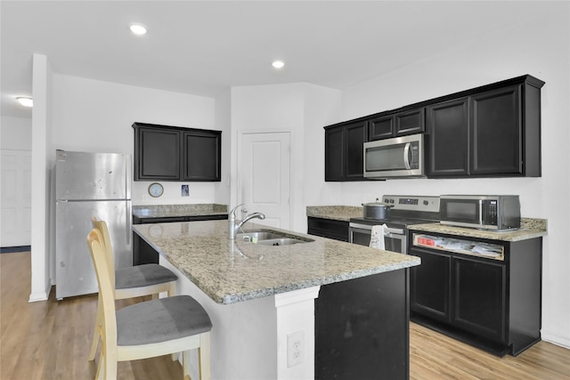 5305 Shady Springs Trl, Fort Worth, TX 76179 - kitchen featuring stainless steel appliances, dark cabinets, light stone counters, a kitchen island with sink, and light wood-style flooring