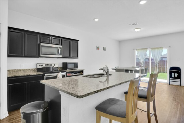 5305 Shady Springs Trl, Fort Worth, TX 76179 - kitchen with appliances with stainless steel finishes, dark cabinets, wood finished floors, a kitchen island with sink, and a breakfast bar