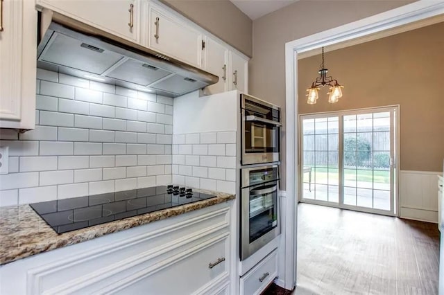 403 Gingerbread Ln, Waxahachie, TX 75165 - kitchen featuring under cabinet range hood, black electric cooktop, a chandelier, white cabinetry, and a wainscoted wall