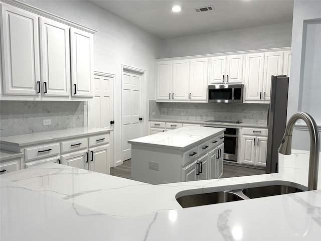 4201 Iron Ln, Mansfield, TX 76063 - kitchen with appliances with stainless steel finishes, backsplash, white cabinets, a center island, and light stone countertops