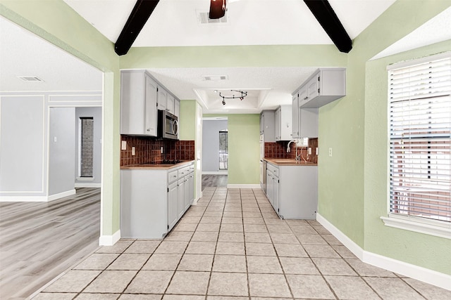 4005 Azalea Ln, Garland, TX 75043 - kitchen with stainless steel microwave, decorative backsplash, a raised ceiling, white cabinets, and beamed ceiling