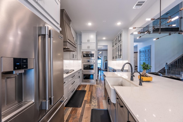 9901 Mi Tierra Dr, Fort Worth, TX 76179 - kitchen featuring stainless steel appliances, dark wood-style floors, custom exhaust hood, glass insert cabinets, and light stone countertops