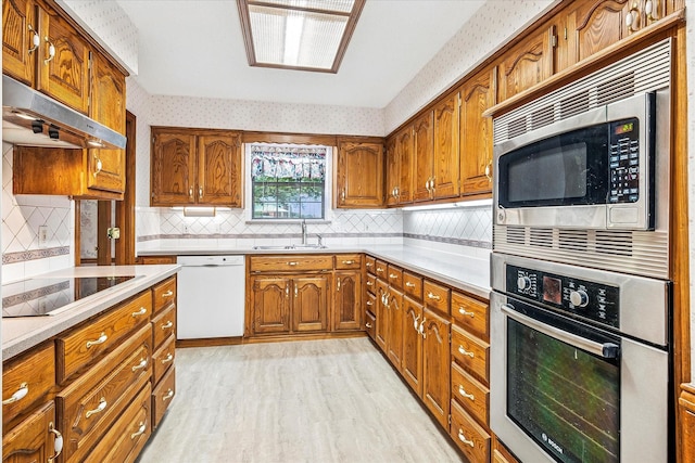 4120 Merriman Dr, Plano, TX 75074 - kitchen with stainless steel appliances, under cabinet range hood, brown cabinetry, light countertops, and wallpapered walls