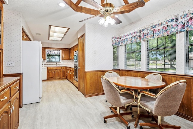 4120 Merriman Dr, Plano, TX 75074 - dining room with wallpapered walls, wainscoting, wooden walls, a ceiling fan, and light wood-style floors