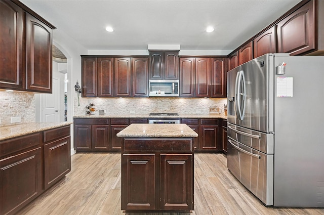 1000 Barn Owl Dr, Little Elm, TX 75068 - kitchen with stainless steel appliances, a kitchen island, light wood finished floors, light stone countertops, and dark brown cabinetry