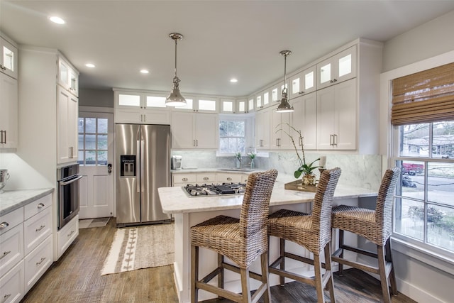 6110 Del Norte Ln, Dallas, TX 75225 - kitchen featuring appliances with stainless steel finishes, wood finished floors, white cabinets, a kitchen bar, and recessed lighting